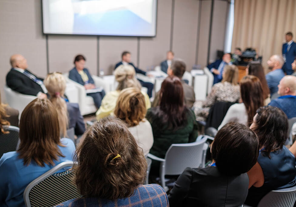 Meeting featuring a diverse audience and professional panelists holding a discussion on stage