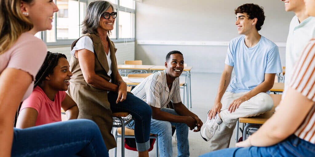 Young group of high school students talking with mature teacher in classroom. Education concept